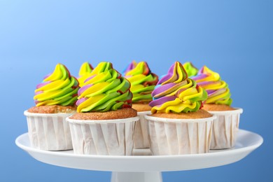 Photo of Tasty cupcakes with colorful cream on light blue background, closeup