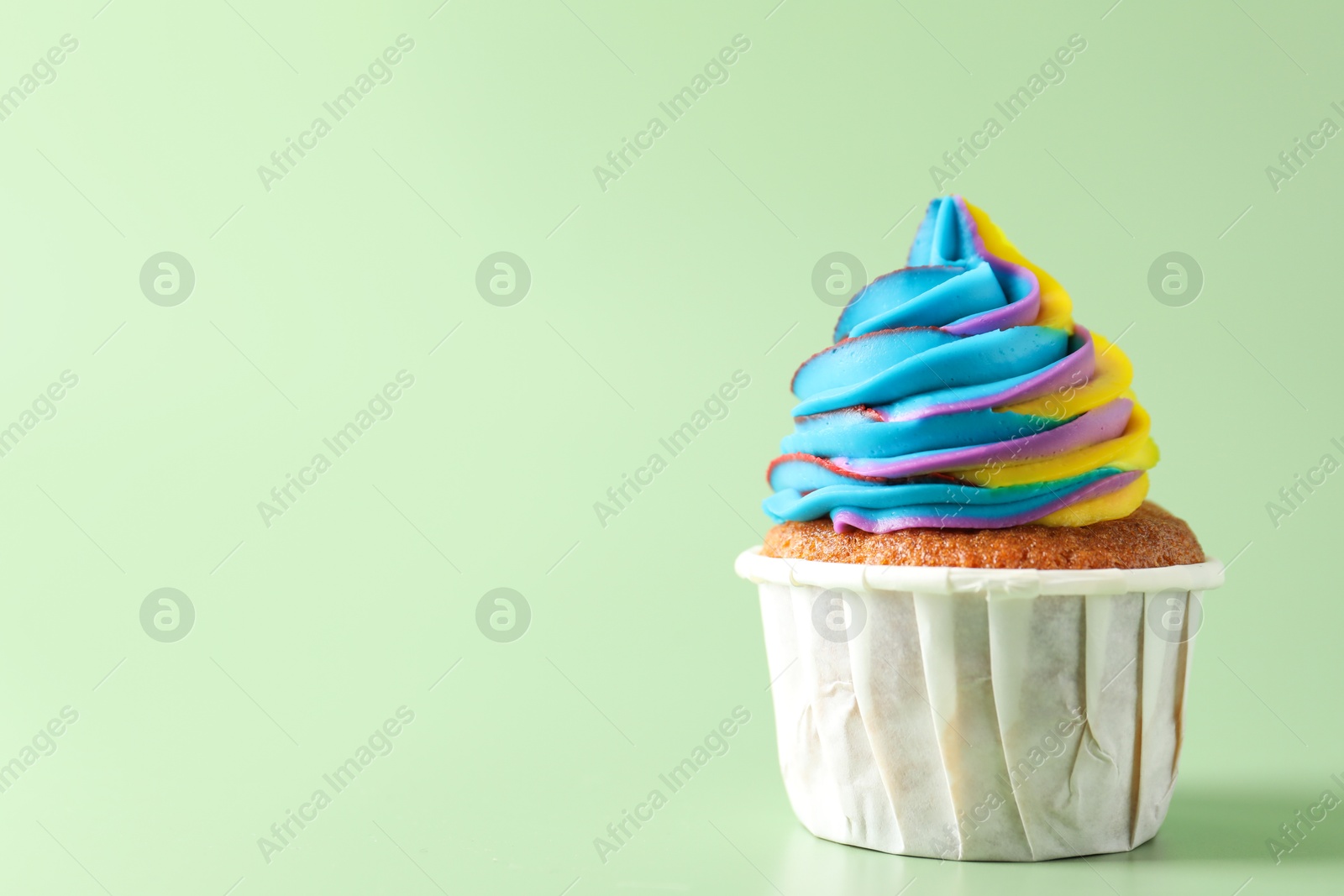 Photo of Tasty cupcake with colorful cream on light green background, closeup. Space for text