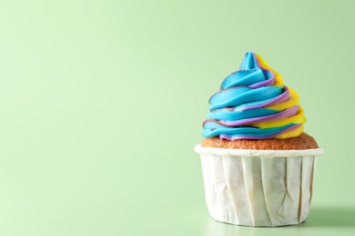 Photo of Tasty cupcake with colorful cream on light green background, closeup. Space for text