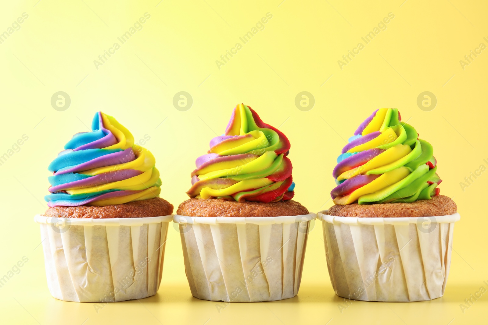 Photo of Tasty cupcakes with colorful cream on yellow background, closeup