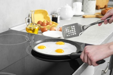 Photo of Woman cooking eggs in frying pan on cooktop indoors, closeup