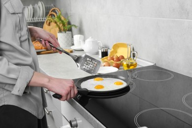 Photo of Woman cooking eggs in frying pan on cooktop indoors, closeup