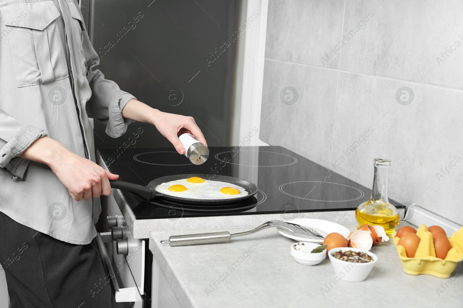 Photo of Woman adding salt into frying pan while cooking eggs on cooktop in kitchen, closeup