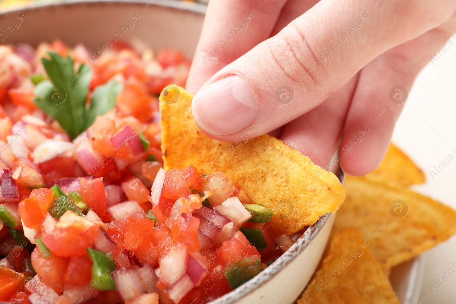 Photo of Woman dipping nacho chip into delicious salsa sauce at table, closeup