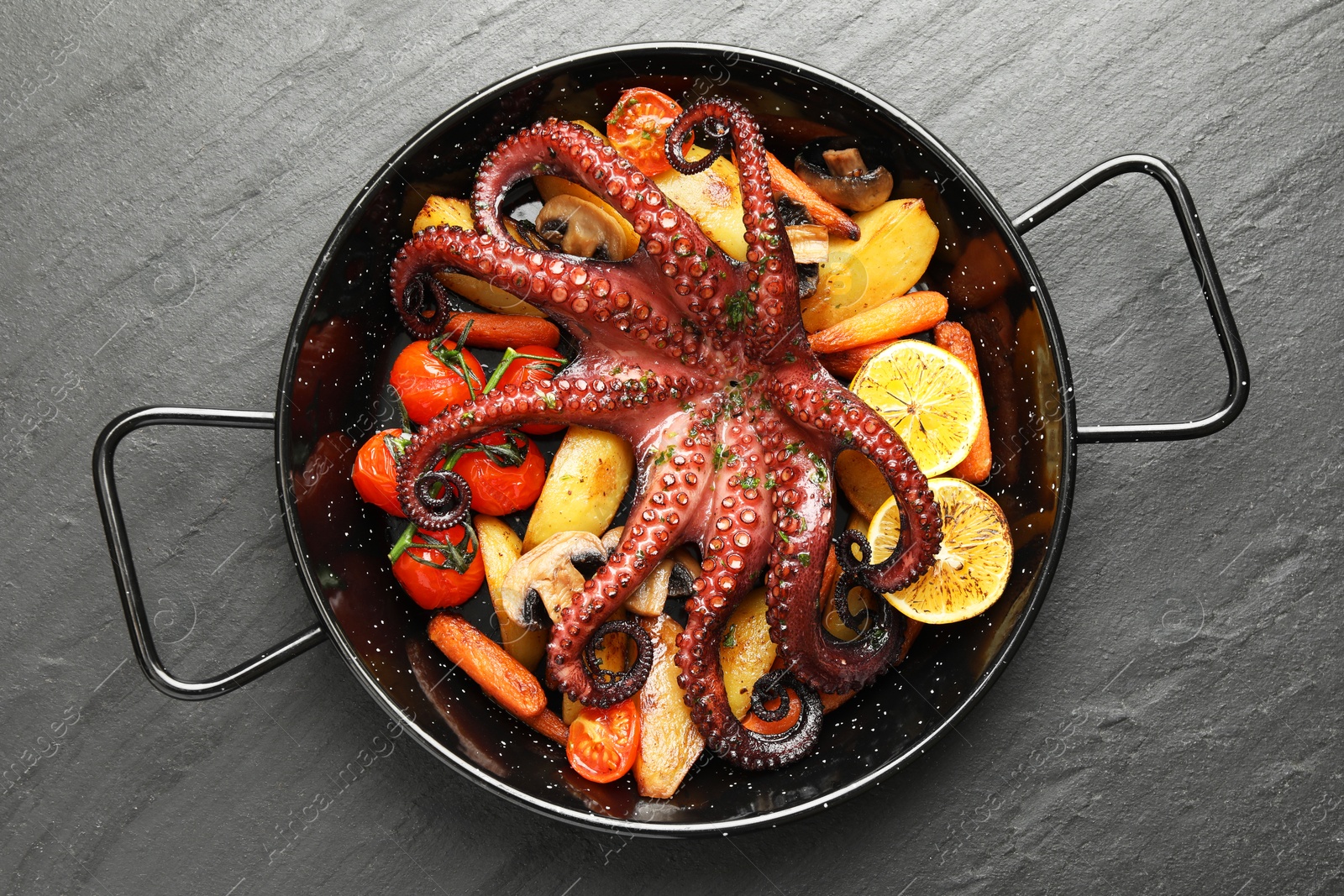 Photo of Fried octopus with lemon, mushrooms and vegetables on grey textured table, top view