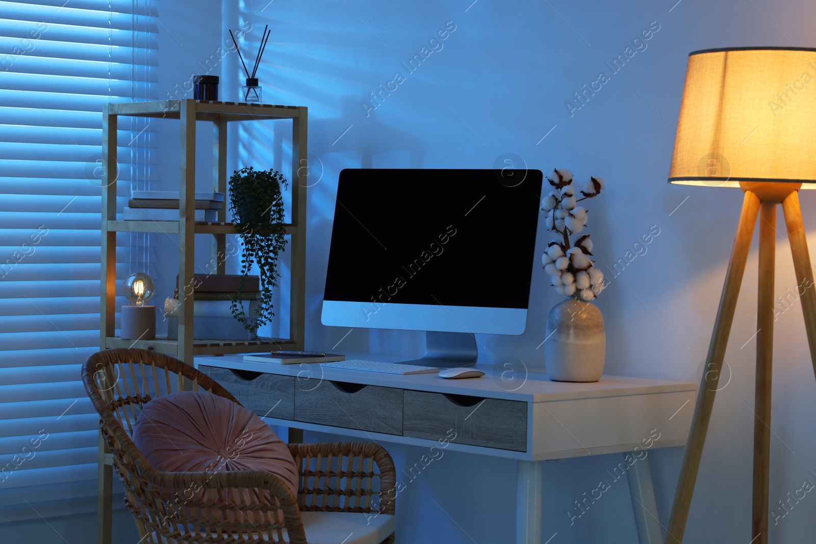 Comfortable workplace with computer on desk and floor lamp at home office in evening Photo of Comfortable workplace with computer on desk and floor lamp at home office in evening