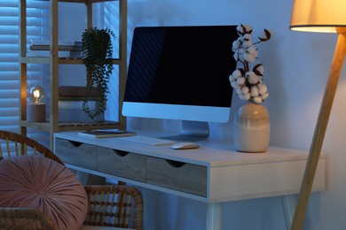 Photo of Comfortable workplace with computer on desk at home office in evening