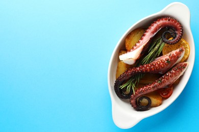 Fried octopus with vegetables, lemon and rosemary in baking dish on light blue background, top view. Space for text