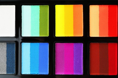 Photo of Bright face paint palette as background, top view