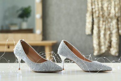 Elegant high heeled shoes and festive lights on white table indoors