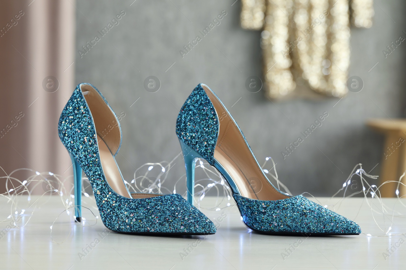 Photo of Elegant high heeled shoes and festive lights on white table indoors