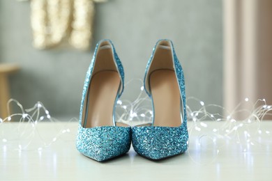 Elegant high heeled shoes and festive lights on white table indoors