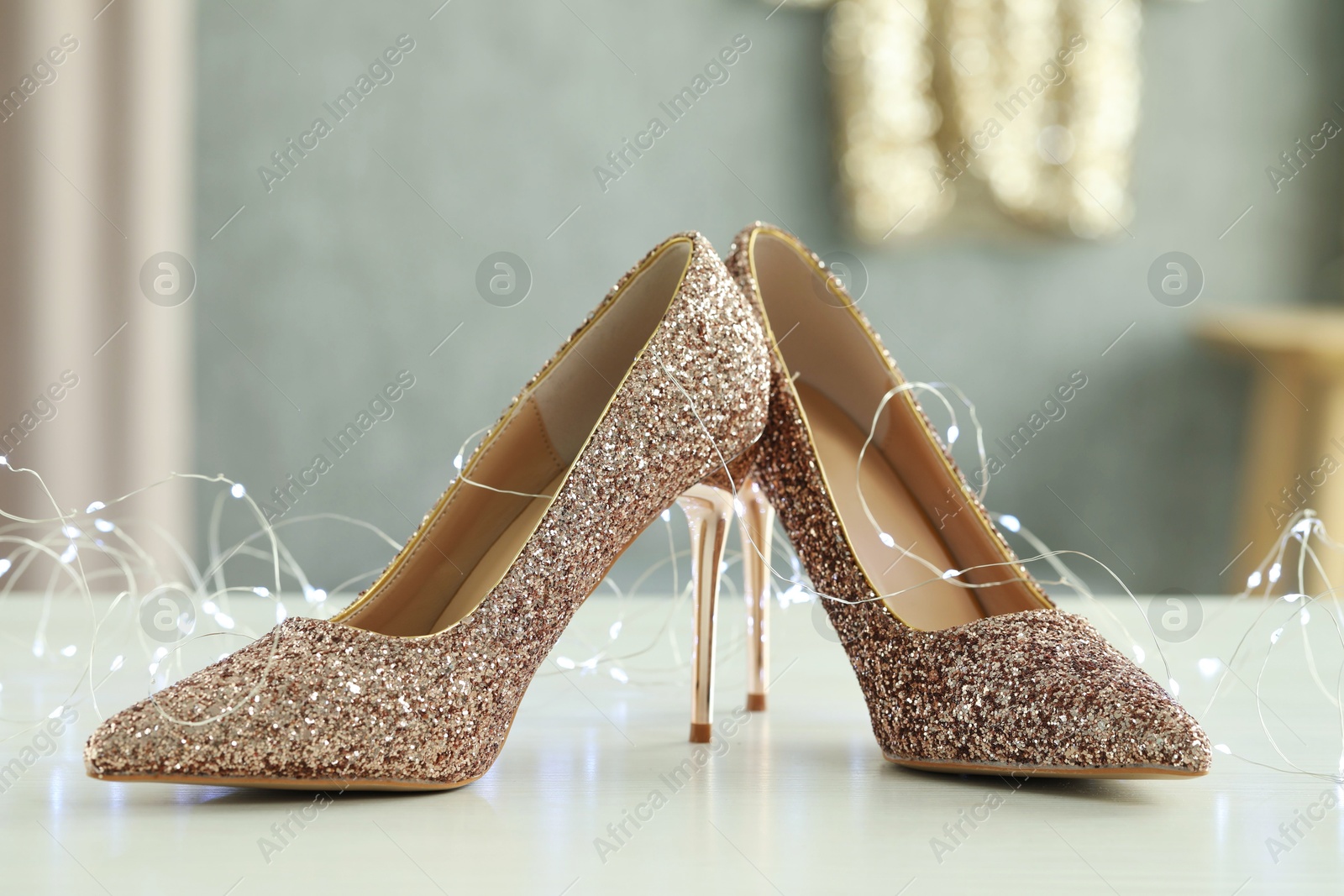 Photo of Elegant high heeled shoes and festive lights on white table indoors