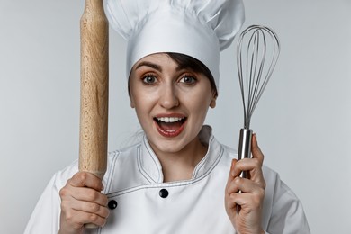 Photo of Excited chef with rolling pin and whisk on light grey background