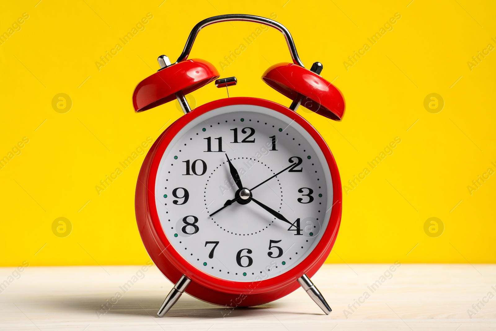 Photo of One red alarm clock on white wooden table against yellow background