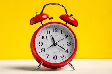 Photo of One red alarm clock on white wooden table against yellow background
