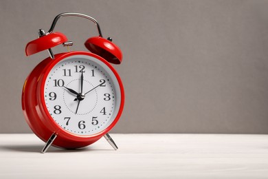 Photo of One red alarm clock on white wooden table against grey background, space for text