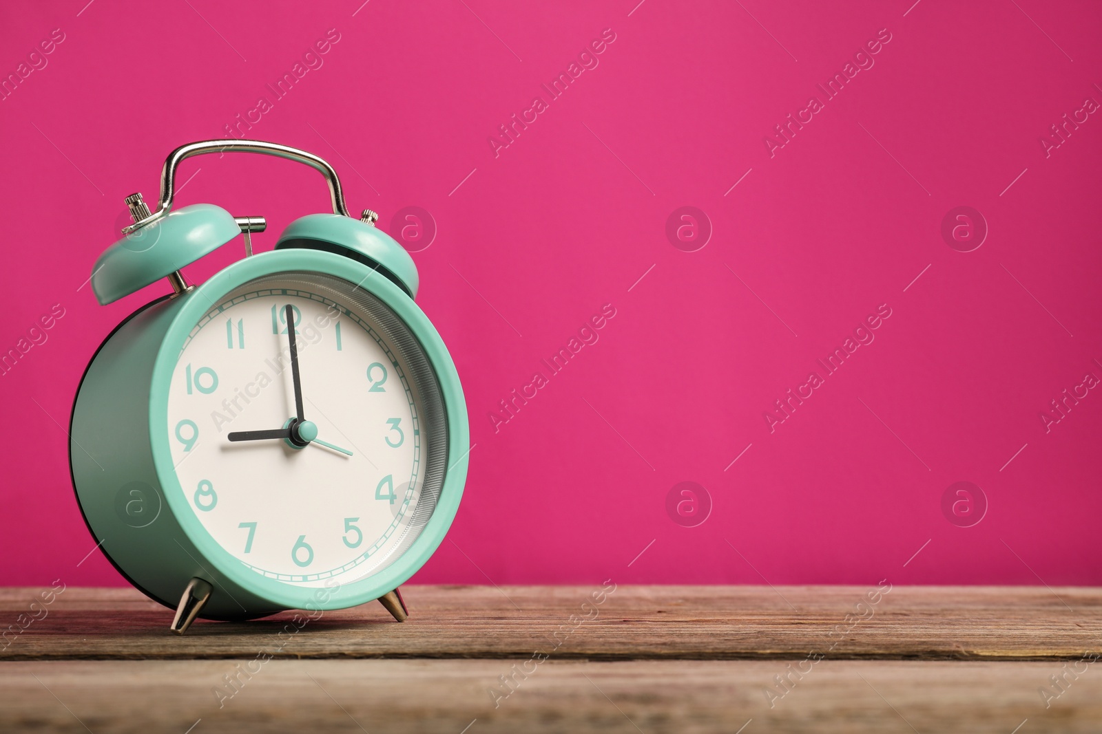 Photo of One turquoise alarm clock on wooden table against bright pink background, space for text