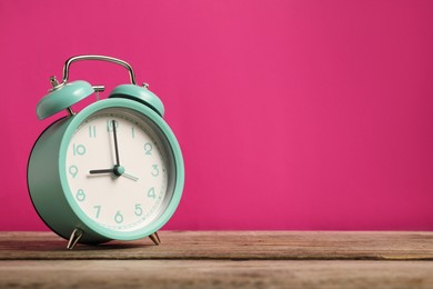 Photo of One turquoise alarm clock on wooden table against bright pink background, space for text