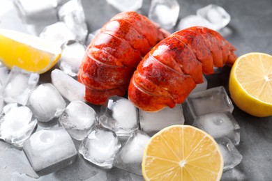 Photo of Tails of boiled lobsters with ice cubes and lemon pieces on grey table, closeup