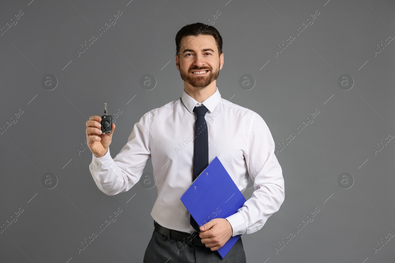 Photo of Cheerful salesman with car key and clipboard on grey background