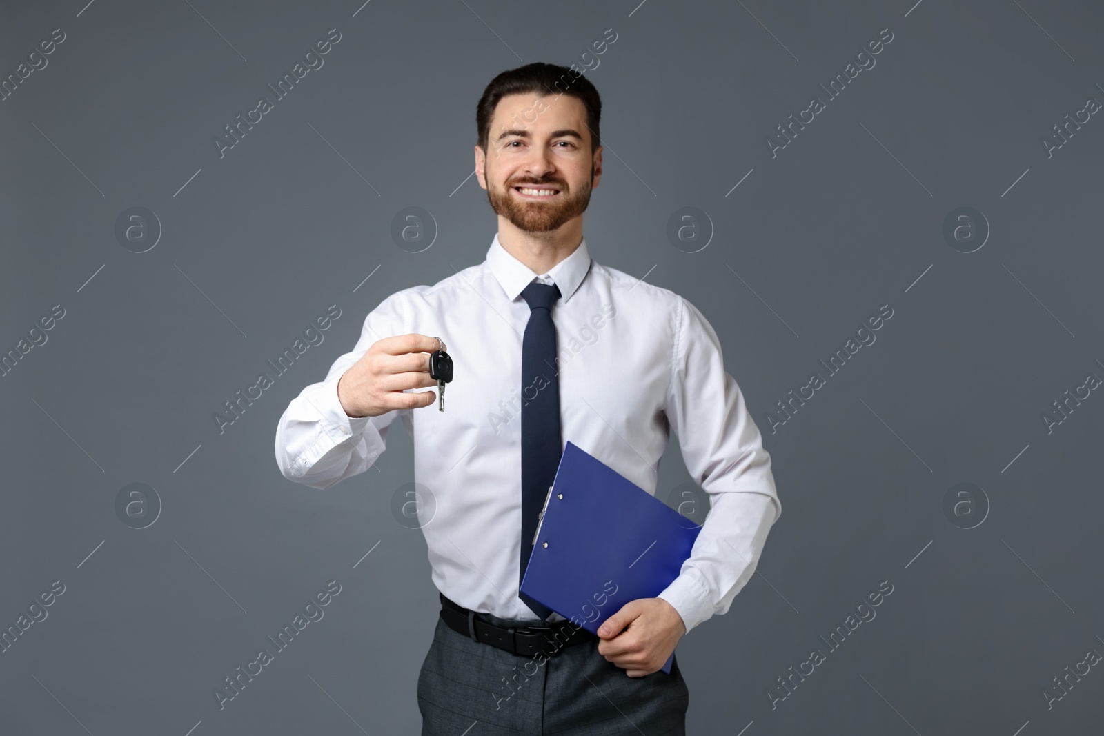 Photo of Cheerful salesman with car key and clipboard on grey background