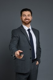 Cheerful salesman with car key on grey background