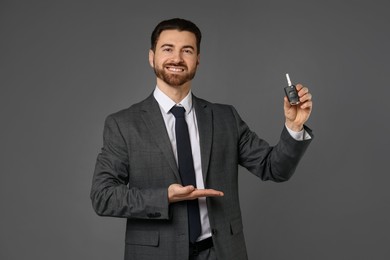 Cheerful salesman showing car key on grey background