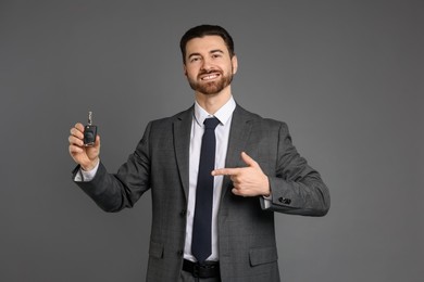 Photo of Cheerful salesman pointing at car key on grey background