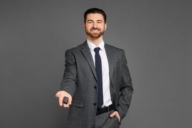 Cheerful salesman with car key on grey background