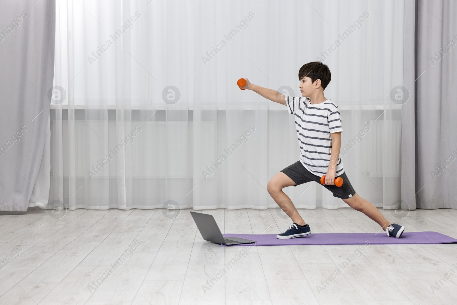 Photo of Little boy exercising with dumbbells near laptop at home, space for text. Morning routine