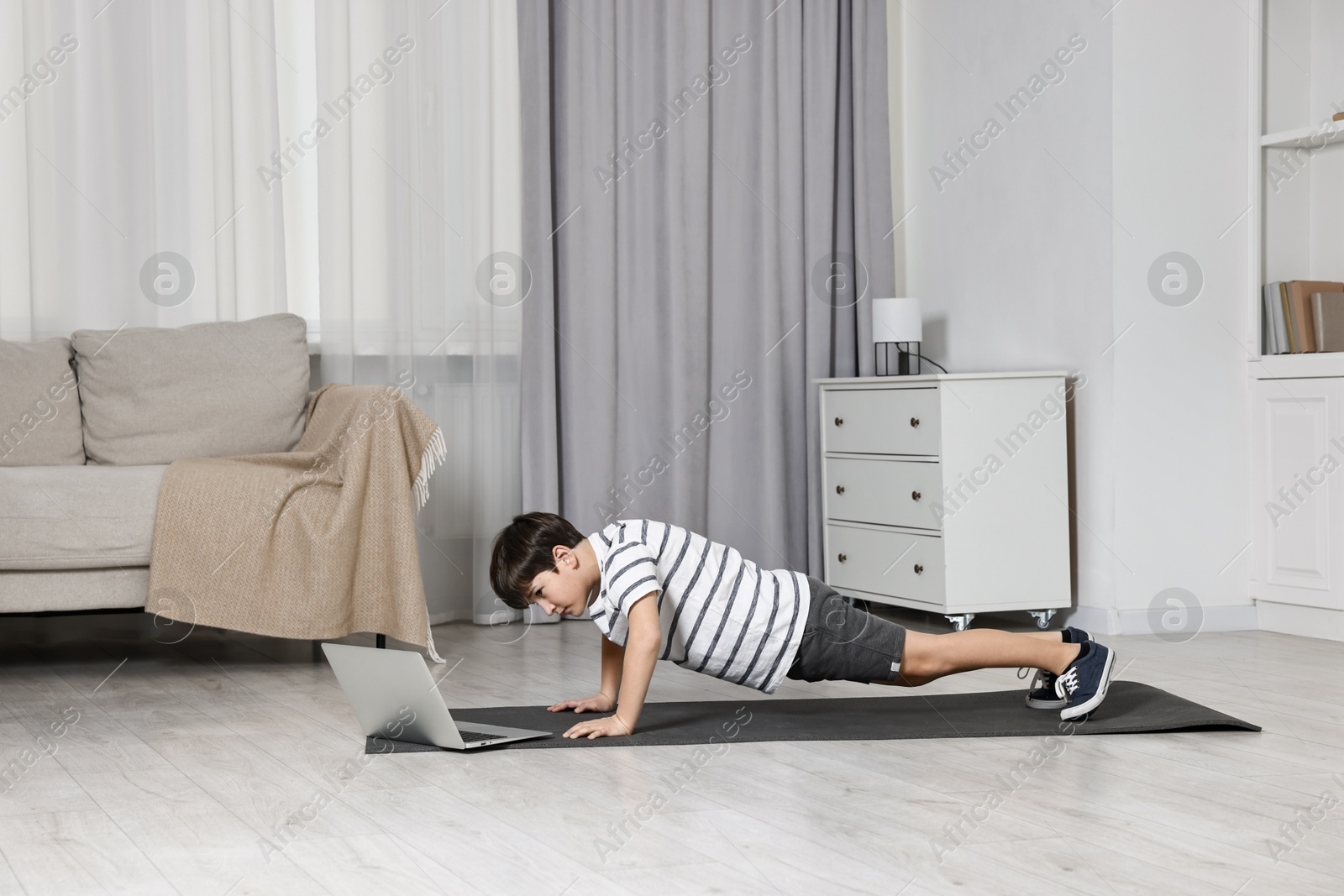 Photo of Little boy exercising near laptop at home. Morning routine