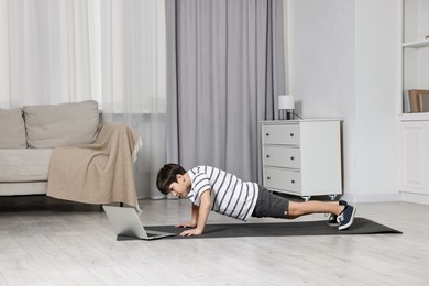 Photo of Little boy exercising near laptop at home. Morning routine