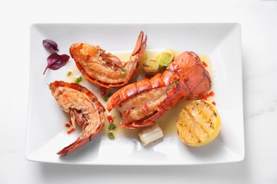 Delicious lobster tails with lemon and green onion on white table, top view