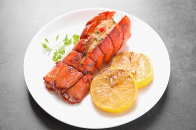 Photo of Delicious lobster tail with microgreens and slices of lemon on grey textured table, closeup