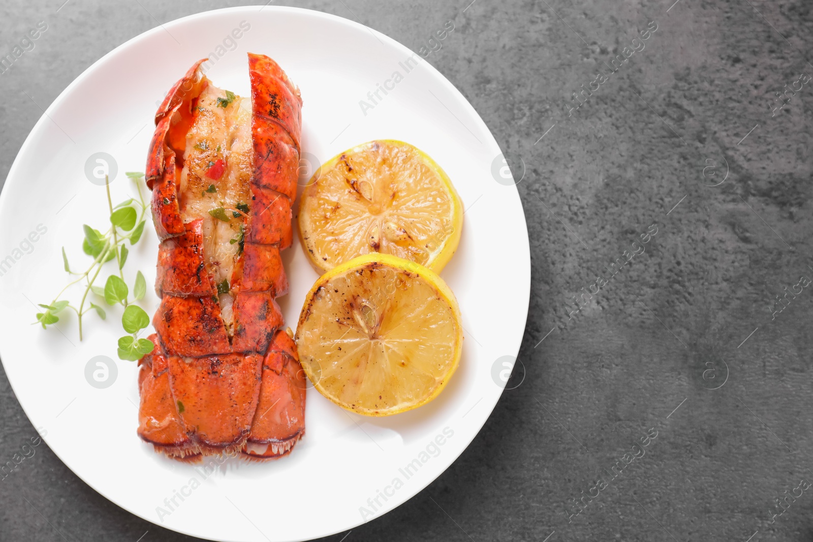 Photo of Delicious lobster tail with microgreens and slices of lemon on grey textured table, top view. Space for text