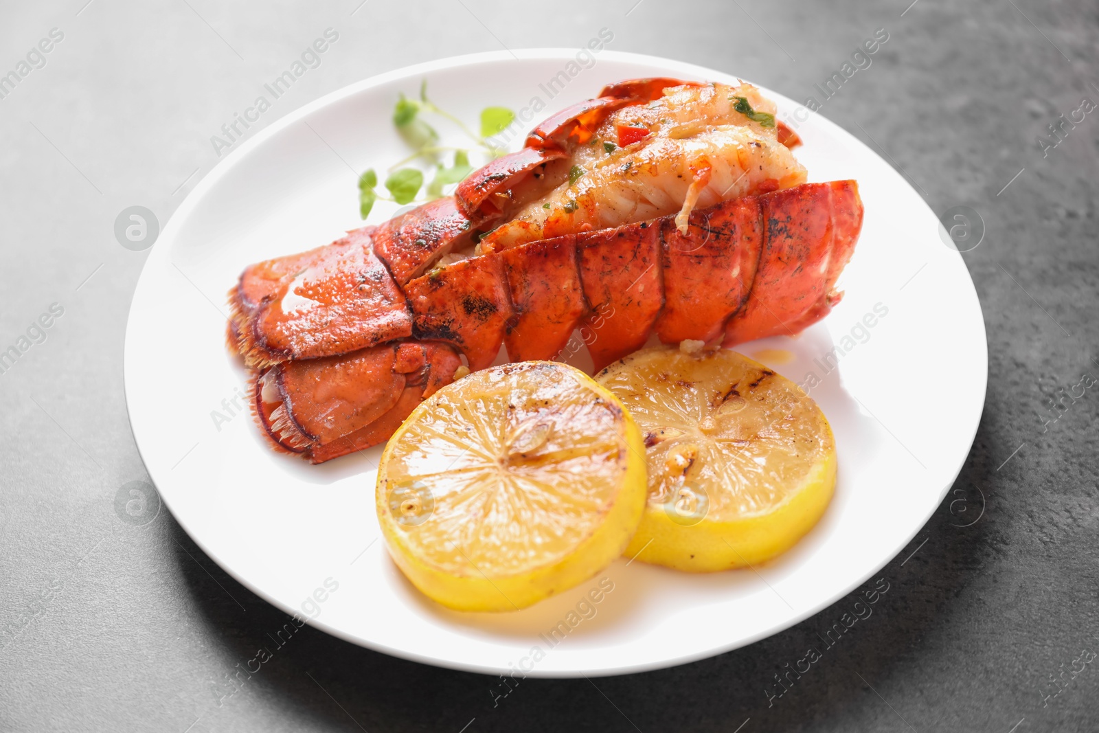 Delicious lobster tail with microgreens and slices of lemon on grey textured table, closeup Photo of Delicious lobster tail with microgreens and slices of lemon on grey textured table, closeup