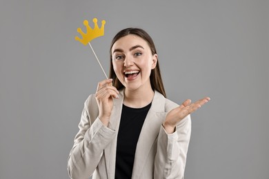 Photo of Happy businesswoman holding stick with paper crown on grey background