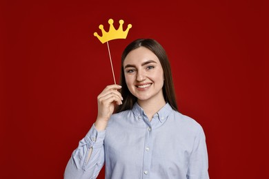 Photo of Happy woman holding stick with paper crown on dark red background