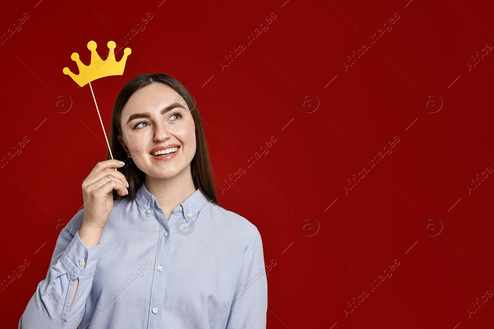 Photo of Smiling woman holding stick with paper crown on dark red background. Space for text