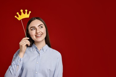 Smiling woman holding stick with paper crown on dark red background. Space for text