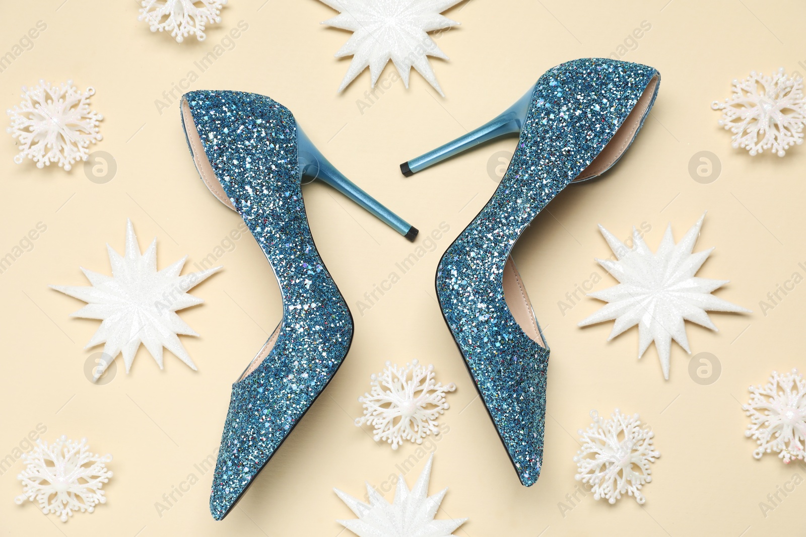 Photo of Shiny high heeled shoes and decorative snowflakes on beige background, flat lay