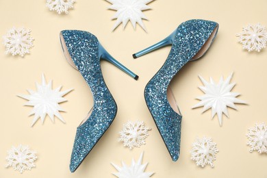 Photo of Shiny high heeled shoes and decorative snowflakes on beige background, flat lay