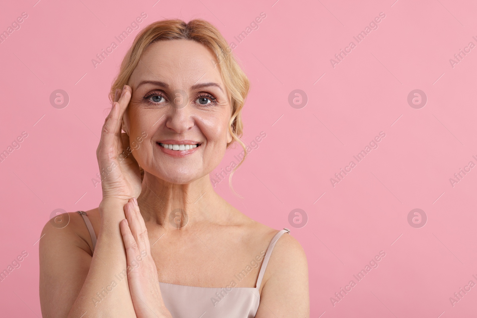 Photo of Smiling middle aged woman on pink background. Space for text