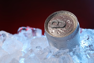 Photo of Refreshing drink in can on ice cubes against dark red background, closeup