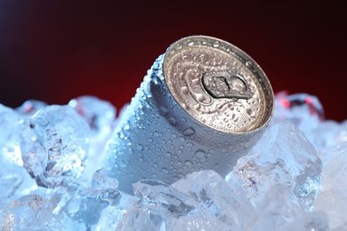 Photo of Refreshing drink in can on ice cubes against dark red background, closeup