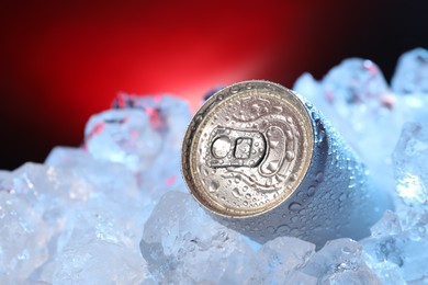 Photo of Refreshing drink in can on ice cubes against dark red background, closeup
