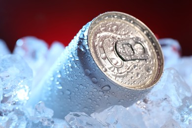 Photo of Refreshing drink in can on ice cubes against dark red background, closeup