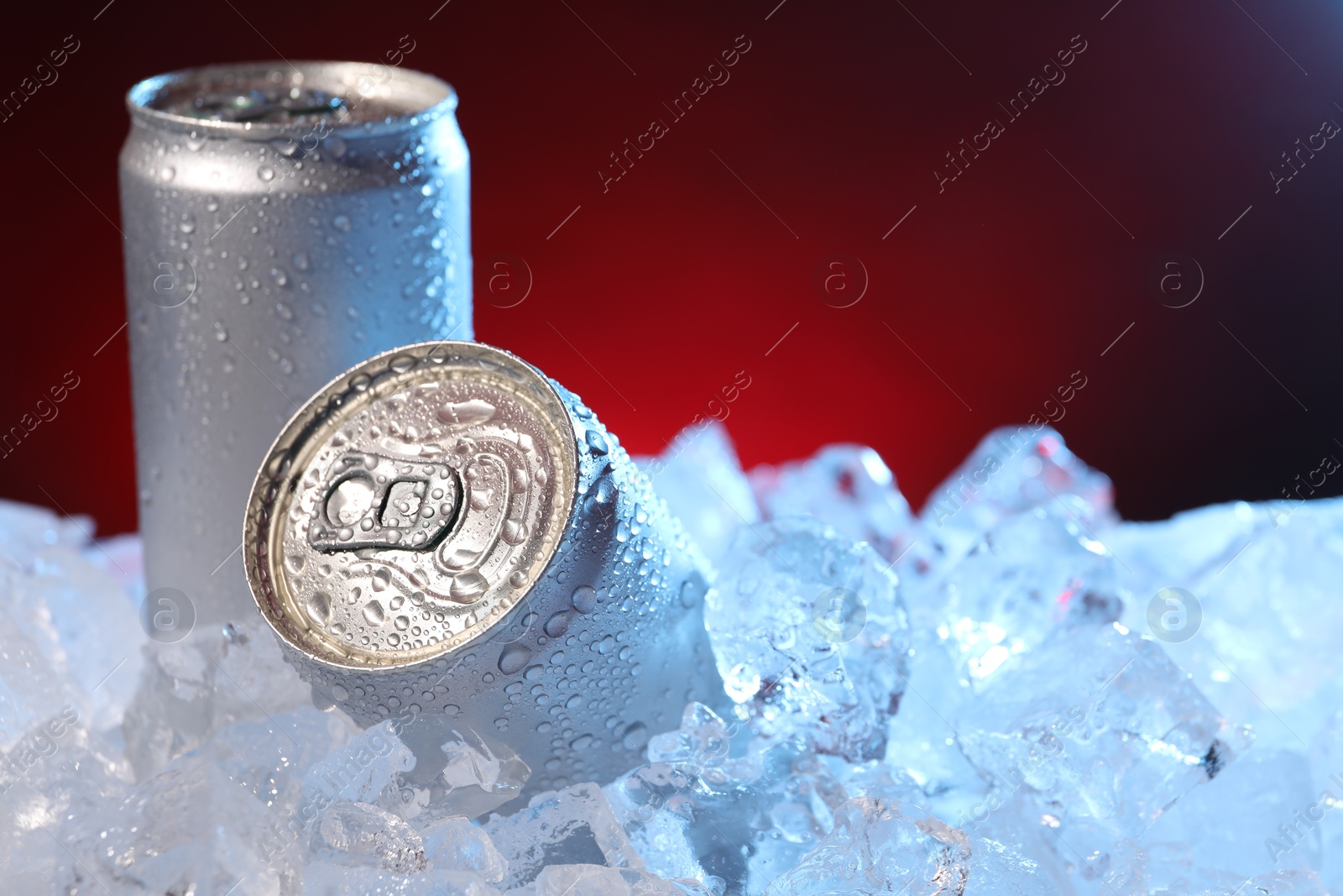 Refreshing drinks in cans on ice cubes against dark red background, closeup Photo of Refreshing drinks in cans on ice cubes against dark red background, closeup