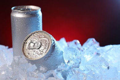 Photo of Refreshing drinks in cans on ice cubes against dark red background, closeup